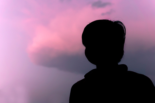 Low angle silhouette portrait of a little boy standing against pink cloudy sky.