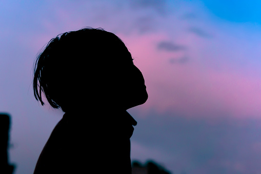 Silhouette image of the little boy looking up and contemplating against blue and pink cloudy sky.