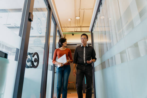 Asian business people having discussion and walk through office corridor Image of Asian businessman and businesswoman having discussion and walk through office corridor malaysia office workers stock pictures, royalty-free photos & images