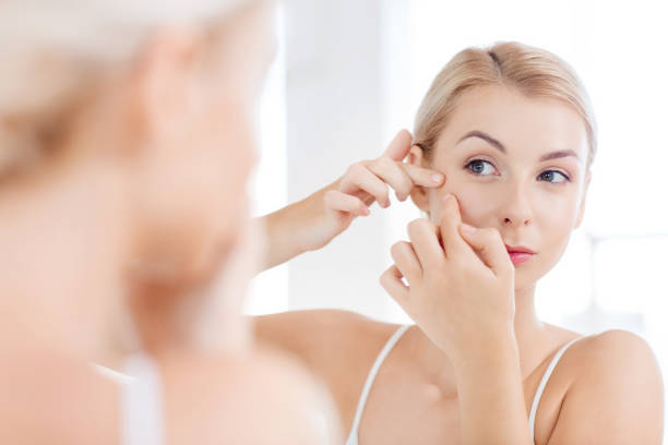istock woman squeezing pimple at bathroom mirror 1318418031