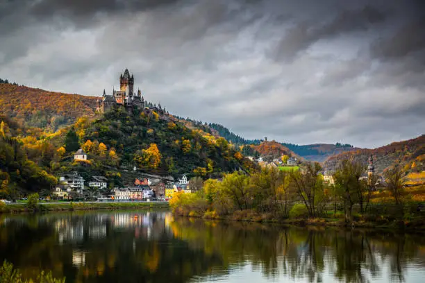 Romantic Moselle river in Germany near Cochem. Beauiful medieval Reichsburg castle on a hill surrounded by colourful autumn forest.