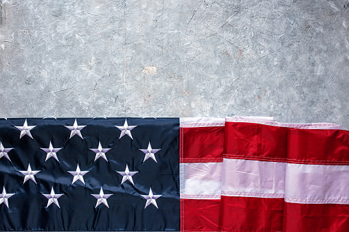 Flag of USA on light grey concrete background.\nEmpty space provided for text placement for US celebrations such as: Memorial Day, Independence Day, etc.