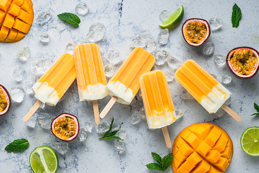 Directly above shot of homemade ice popsicles. Mango, passion fruit, limes, mint leaves with freshly make popsicles on ice cubes.