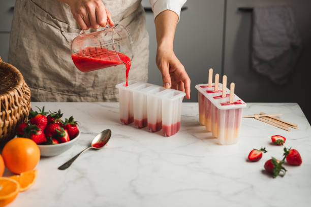 Filling liquid ice cream mix in moulds Female preparing mix fruit ice cream with plastic moulds in kitchen with ingredients on table. Hand of a woman filling liquid ice cream mix into candy moulds. homemade icecream stock pictures, royalty-free photos & images