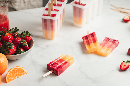 Orange and strawberry ice cream on stick. Delicious mix fruit ice cream candy bars on table with strawberries and oranges on kitchen table, with plastic ice cream moulds.