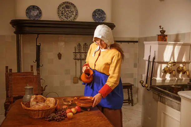 Portrait of a beautiful historical dutch milk maid wearing historically correct outfit in a typical townhouse kitchen