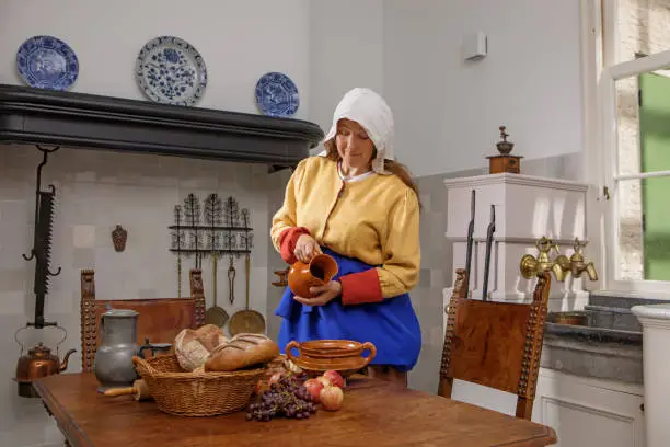 Portrait of a beautiful historical dutch milk maid wearing historically correct outfit in a typical townhouse kitchen