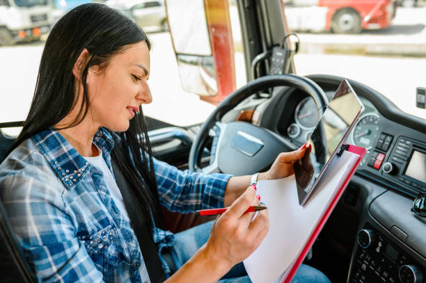 Female truck driver using a mobile app and writing on a clipboard