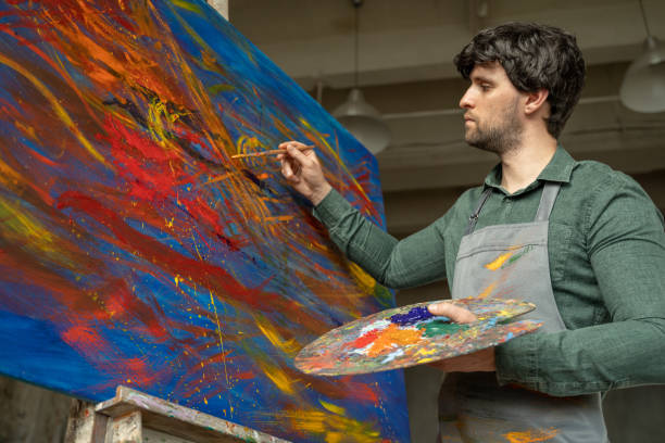 el hombre es un artista, sosteniendo un pincel y dibujando una imagen abstracta - colores fotos fotografías e imágenes de stock