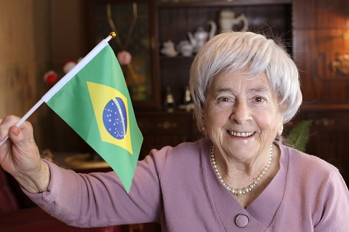 Senior woman holding the Brazilian flag at home.