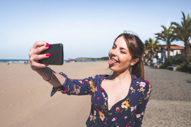 istock Young woman taking a selfie with a mobile phone at the beach side 1318436522