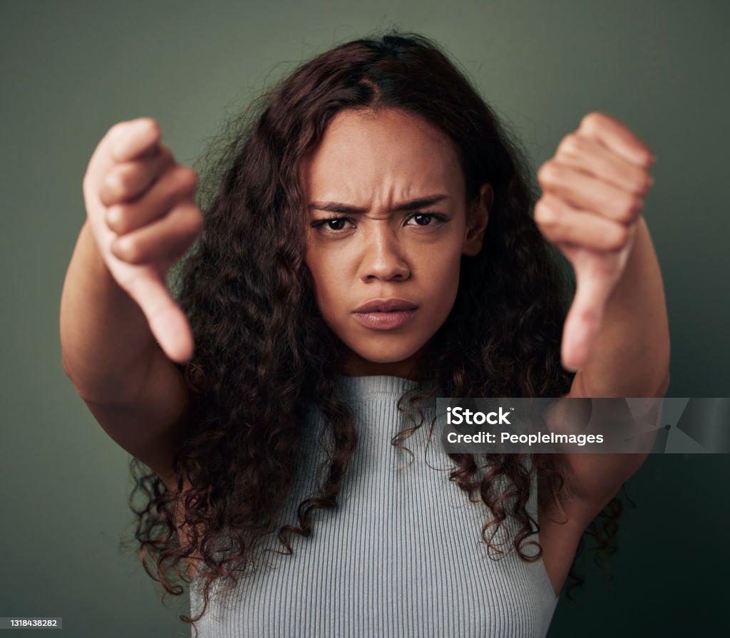 Studio shot of a young woman showing thus down against a green background That's not how we do things around here Thumbs Down Stock Photo