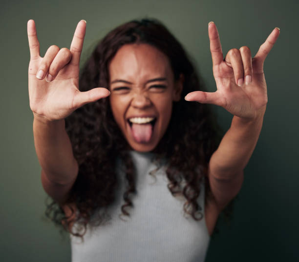 Studio shot of a young woman making a rock n’ roll gesture against a green background Rock on, you rebels! rock musician stock pictures, royalty-free photos & images