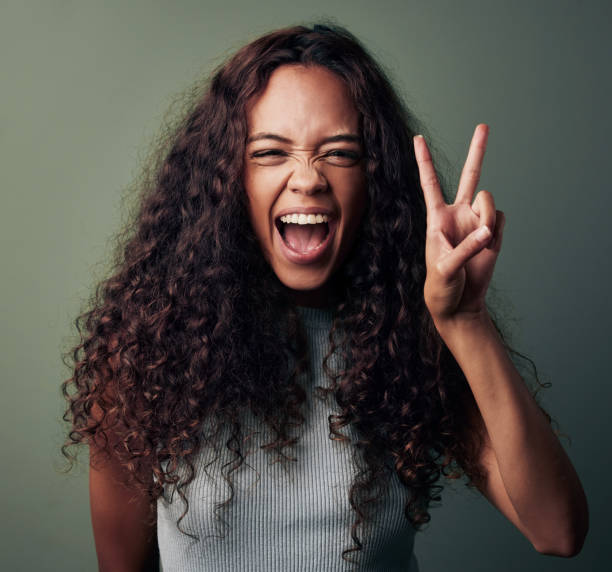 Studio shot of a young woman making a peace gesture against a green background Let's make peace go viral! v sign stock pictures, royalty-free photos & images