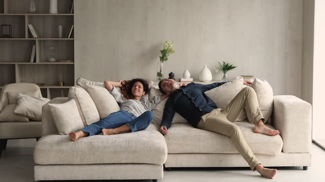 Happy couple jumping on comfy soft sofa laughing enjoy relaxation