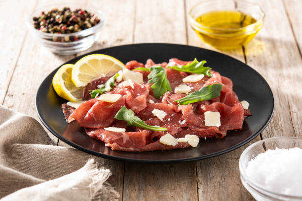 Marbled beef carpaccio on black plate Marbled beef carpaccio on black plate on wooden table carpaccio parmesan cheese beef raw stock pictures, royalty-free photos & images
