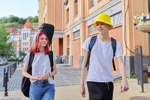 Urban modern lifestyle, handsome creative youth. Fashionable teenagers couple guy and girl walking together along the city street, hipster female with guitar in case