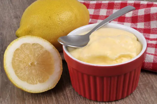 Lemon cream ramequin with a checkered towel and a lemon in close-up on a wooden background