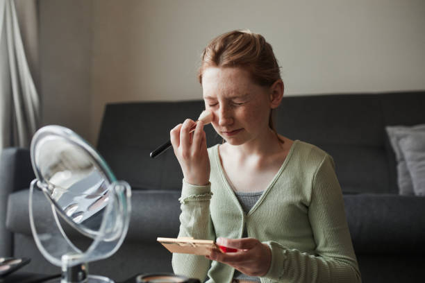 istock Girl looking at the mirror and preparing makeup with a powder and brush while playing 1318450398