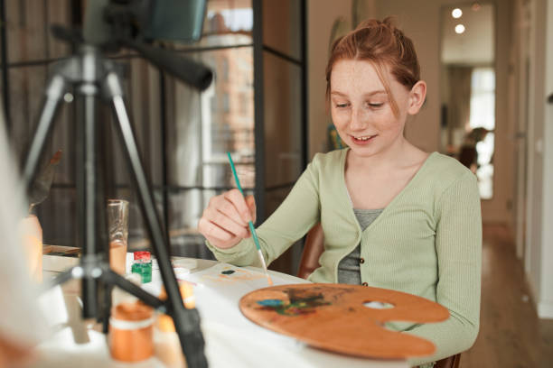 istock Girl looking at the smartphone camera and holding brush while making online translation 1318450521