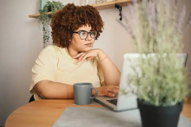 Photo of Attractive happy stylish plus size African black woman student afro hair in glasses studying online working on laptop computer at home office workspace. Diversity. Remote work, distance education.