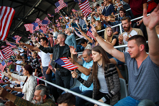 USA colored flags waving above large crowd on a stadium sport match.