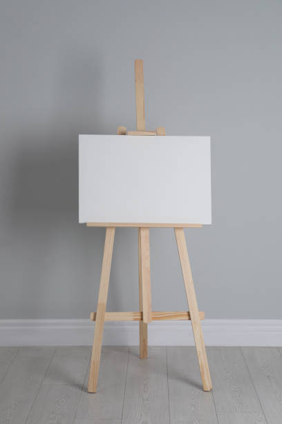 istock Wooden easel with blank canvas near light wall 1318458357