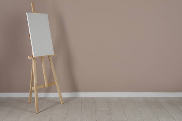 istock Wooden easel with blank canvas near beige wall. Space for text 1318458396