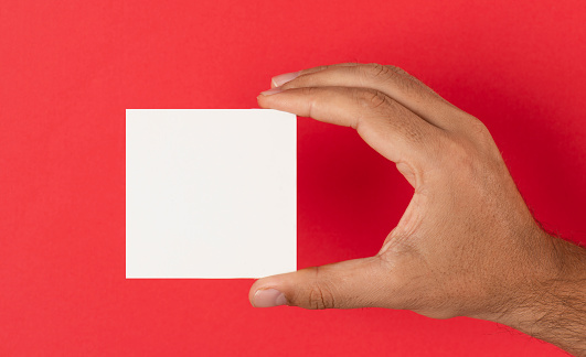 Man holding blank square card in front of a red background.