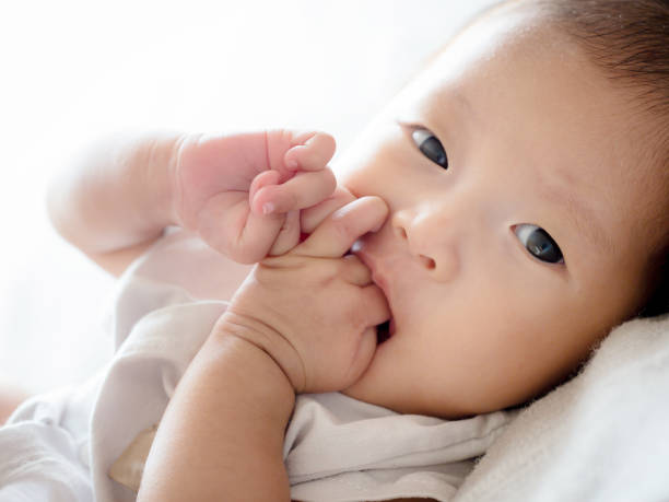 クローズアップ幼児アジアの女の赤ちゃんはリラックスしたり、空腹のためにサインするために彼女の指を吸う - finger in mouth 写真 ストックフォトと画像