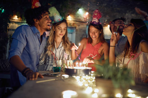 group of cheerful friends lighting candles on the birthday cake at the open air party. quality friendship time together - city night lighting equipment mid air imagens e fotografias de stock