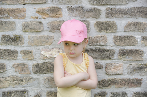 Portrait of displeased little girl wearing pink summer cap and yellow shirt