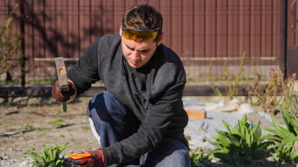 istock Defocus young construction worker in yellow glasses removing irregularities on floor screed with hammer and chisel. Male hands in red work gloves smash the concrete slab. Patio at home. Out of focus 1318462524