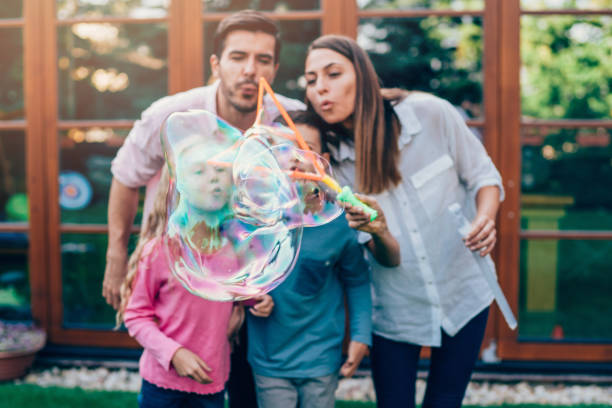 family having fun in backyard with soap bubbles. - bubble child bubble wand blowing imagens e fotografias de stock