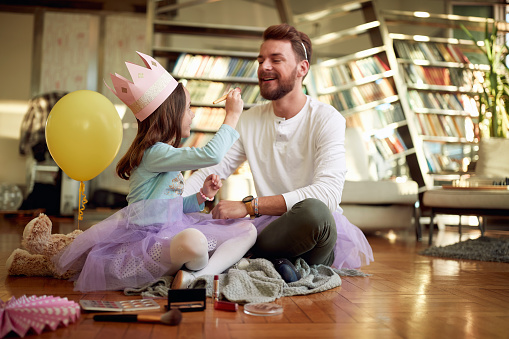 A young father and his little daughter sitting on the floor in a relaxed atmosphere at home and preparing for a ballet practice. Family, together, home