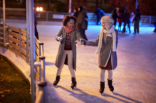 Female friends holding hands while skating at ice rink on a beautiful magical night. Skating, friendship, together