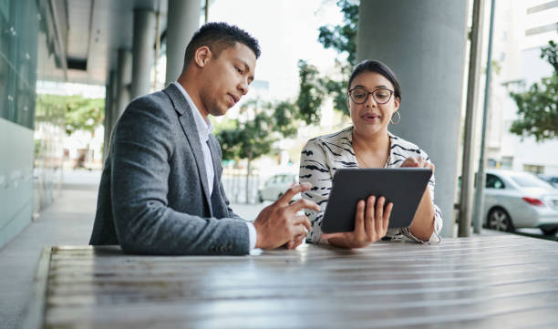 istock Two young businesspeople discussing work on a tablet outside at a table 1318469480