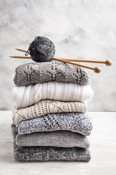 istock Stack of cozy knitted sweaters and pullovers with knitting needles on wooden background 1318471176