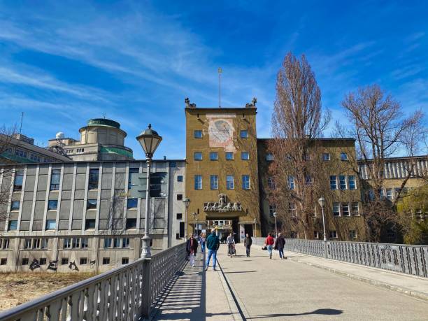 Germany, Munich - March, 2021: People walking on the bridge over River Isar in the center of Munich in front of Deutsches Museum buildings on a sunny spring day.