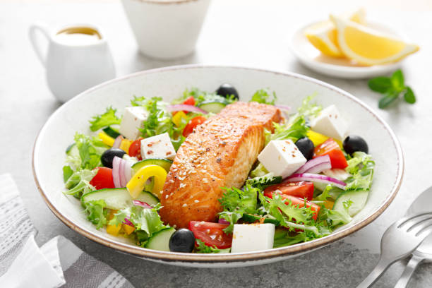 Salmon fish salad. Fresh vegetable greek salad with tomato, pepper, lettuce, olives, cucumbers, feta cheese and grilled salmon fish fillet in bowl, healthy food, omega 3, keto diet, mediterranean cusine. ensalada de pescado de salmón. ensalada griega de verduras frescas con tomate, pimienta, lechuga, aceitunas, pepinos, queso feta y filete de pescado de salmón a la parrilla en tazón, alimentos saludables, omega 3, dieta keto, cusino mediterráneo.