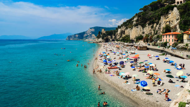 Vacationers on the free sandy and pebble Capo San Donato or Castelleto Pier Beach on a summer, sunny day near the calm Mediterranean Sea. Finale Ligure, Italy - 22 july 2019: Vacationers on the free sandy and pebble Capo San Donato or Castelleto Pier Beach on a summer, sunny day near the calm Mediterranean Sea. Ligurian Riviera coast. finale ligure stock pictures, royalty-free photos & images