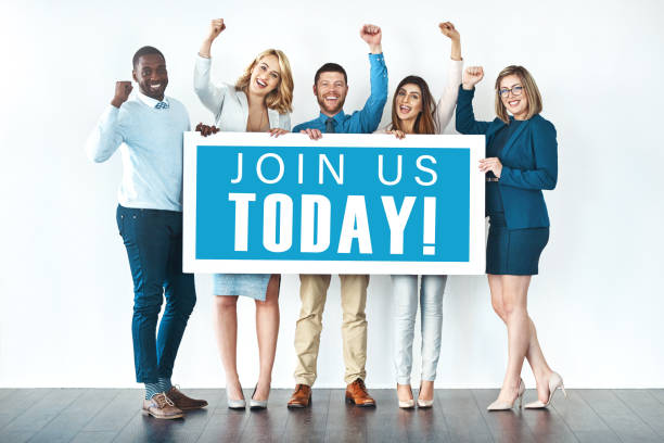 Studio shot of businesspeople holding up a sign with the words “join us today” on it and cheering We want you on our team! help wanted sign photos stock pictures, royalty-free photos & images