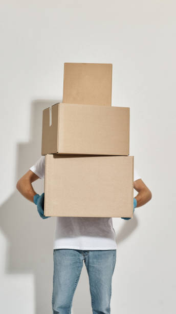 istock Young redhead deliveryman holding three cardboard boxes standing one on one 1318475277