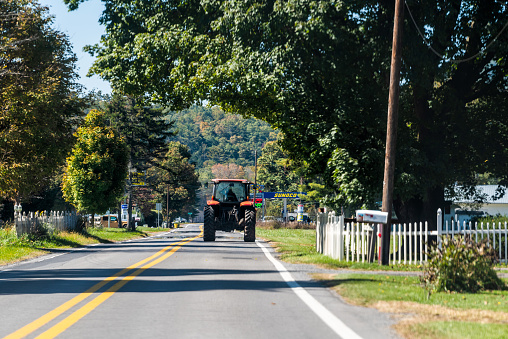 Green Bank, USA - October 6, 2020: Farmer tractor driving on paved rural countryside highway road in Green Bank city small science town village in West Virginia
