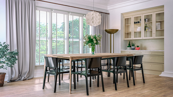 Dining room with table, chairs, pendant lights and decoration on hardwood floor in front and large windows with curtains and blinds in background. Built-in beige cabinets with glass doors and drawers for cutlery and plates. 3D rendered image.