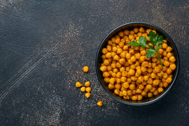 istock Fried chickpeas with turmeric with parsley and lime in black plate on an old black table background. Roasted spicy chickpeas or Indian chana or chole, popular snack recipe. Top view. 1318480446