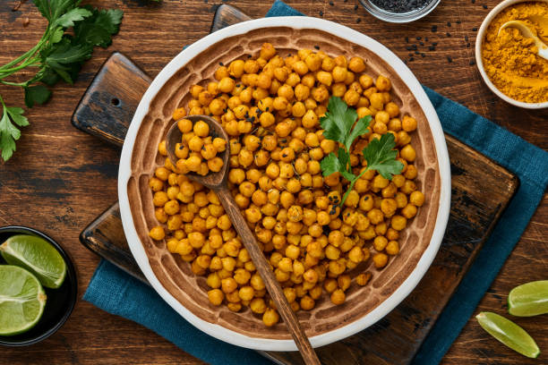 istock Fried chickpeas with turmeric in ceramic plate on an old wooden table background. Roasted spicy chickpeas or Indian chana or chole, popular snack recipe. Top view. 1318480540