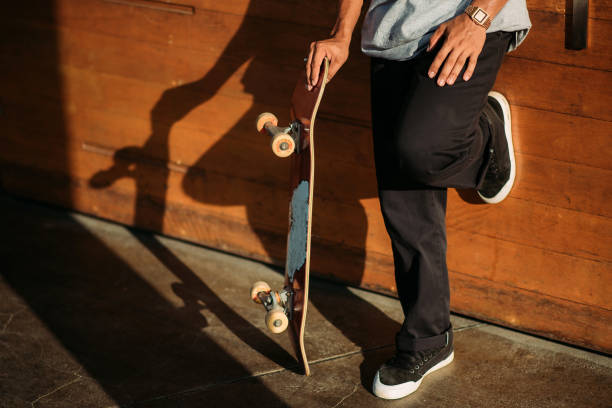 Asian male skateboarder taking a break and leading on wall in a skate park stock photo