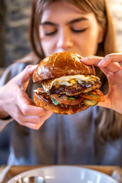 istock Big appetizing burger with meat in female hands in a cafe. 1318483608