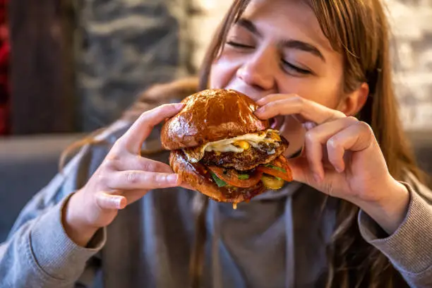 Photo of Big appetizing burger with meat in female hands in a cafe.